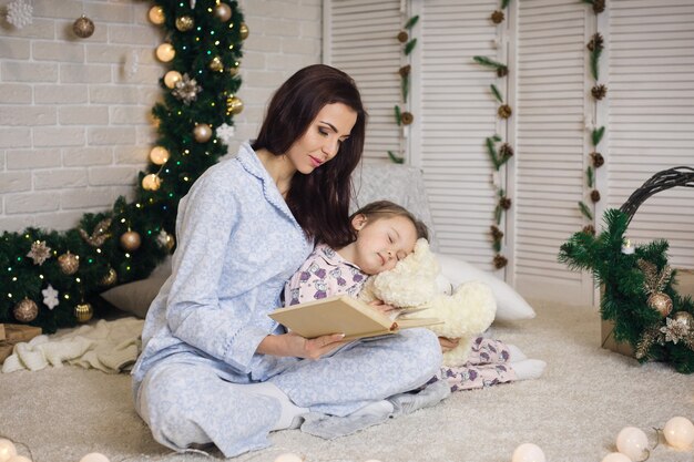 Matka czytanie książki do jej córeczki słodkie w pobliżu choinki w domu