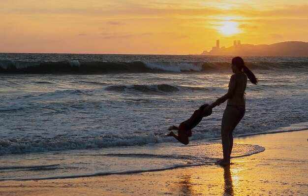 Matka huśtająca syna na brzegu plaży podczas zachodu słońca