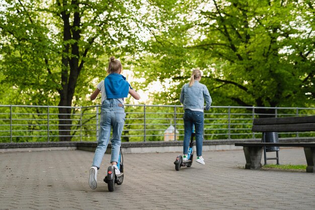 Matka i córka jeżdżą na skuterach elektrycznych w parku miejskim