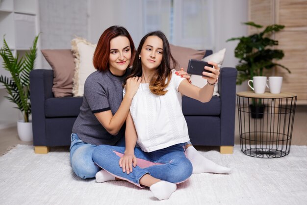 Matka i córka robią sobie zdjęcie selfie smartfonem w salonie
