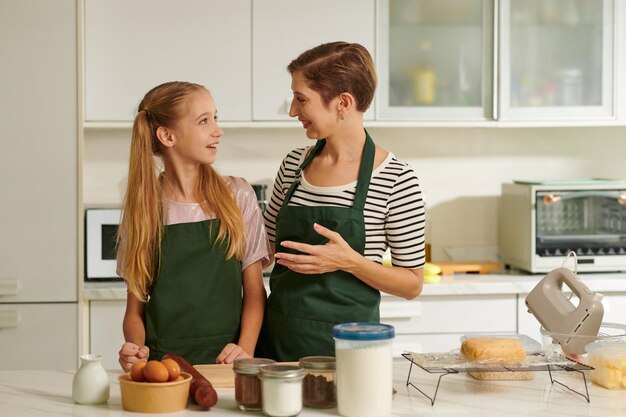 Matka i córka stoją przy blacie kuchennym i omawiają przepis na pierniki