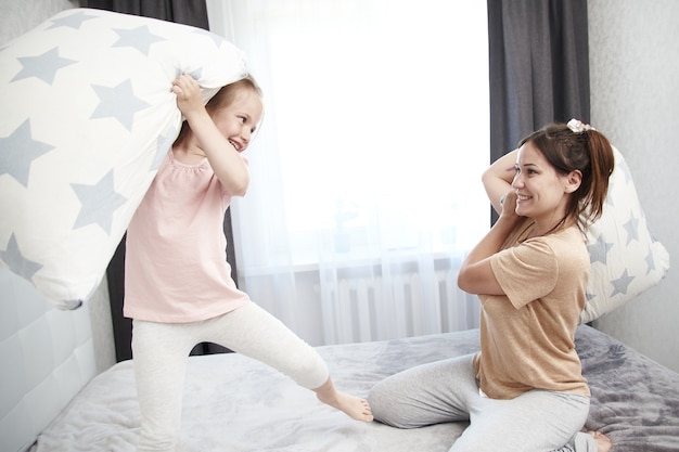 Matka i córka walczą z poduszkami i śmieją się.