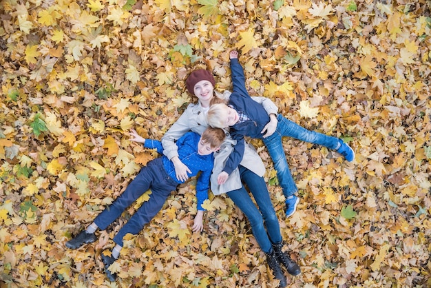 Matka i dwóch synów leżących na liściach jesienią w lesie. Młoda rodzina w parku. Widok z góry.