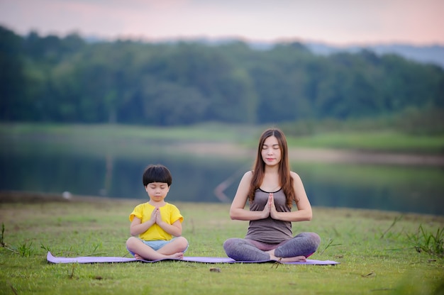 Matka i dziecko robi ćwiczenia jogi na trawie w parku przed zachodem słońca w lecie.
