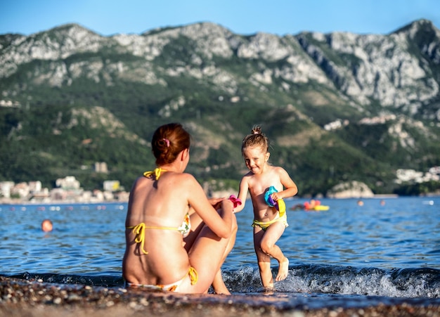 Matka i dziewczynka bawią się na piaszczystej plaży z morzem w tle Becici Czarnogóra