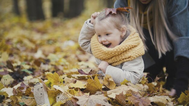 Matka i jej córka mała dziewczynka bawią się w jesiennym parku - rzucaj liśćmi, śmiech dziecka, zbliżenie