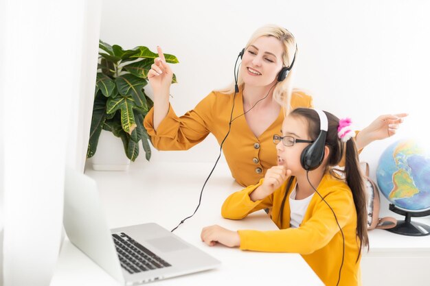 Zdjęcie matka i jej córka słuchają muzyki na laptopie, siedzą w salonie, w naturalnym świetle.