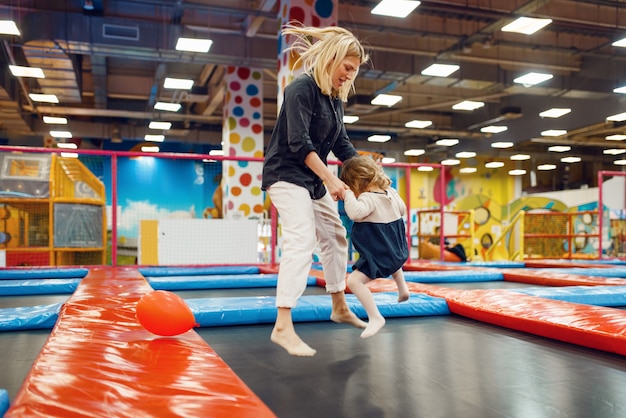 Matka i mała dziewczynka skoki na trampolinie w centrum rozrywki. Mama i córka wyjeżdżają na wakacje, szczęście z dzieciństwa, szczęśliwe dzieciaki na placu zabaw