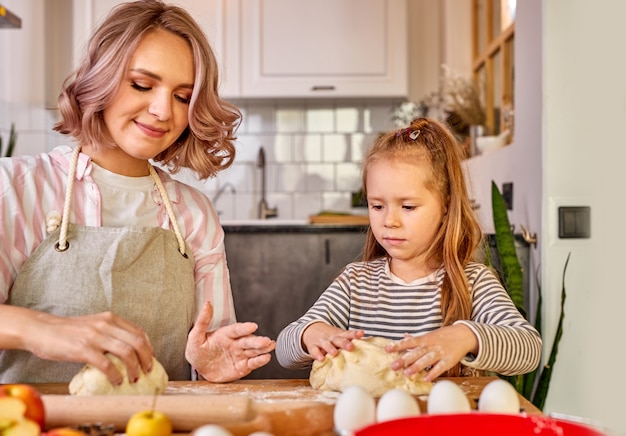 Matka i mała urocza córka gotują razem w kuchni, piękna mama uczy uroczą dziewczynkę wyrabiania ciasta na domowe ciasto, przygotowując niespodziankę dla rodziny