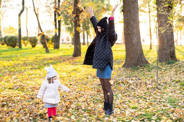 Matka i młoda dziewczynka o blond włosach bawią się w jesiennym parku na tle żółtych i pomarańczowych liści Rodzina spaceruje po parku