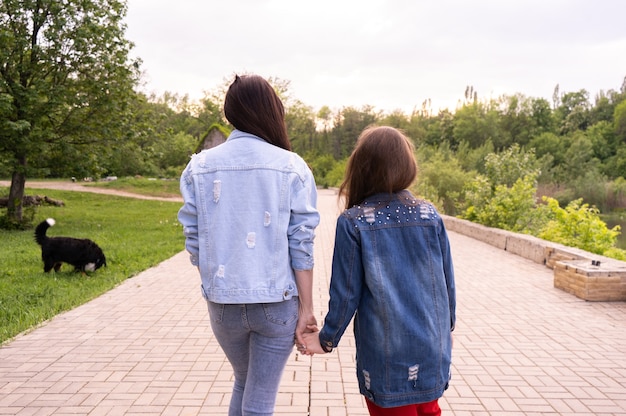 Matka i nastoletnia córka spaceru w parku, trzymając się za ręce, szczęśliwa młoda kaukaska kobieta z długimi włosami i nastolatką spędzającą czas w mieście, styl życia rodziny