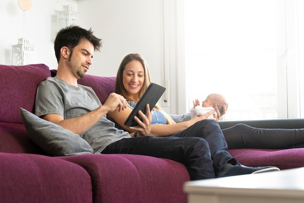 Matka i ojciec z noworodkiem na kanapie surfują po Internecie za pomocą cyfrowego tabletu