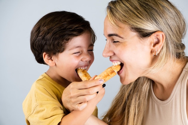 Matka i syn cieszą się i jedzą latynoamerykańską przekąskę o nazwie tequenos. Śmieszne wyrazy twarzy