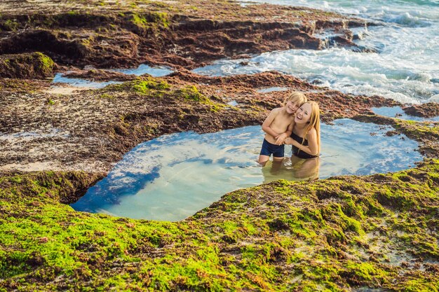 Zdjęcie matka i syn turyści na plaży pantai tegal wangi siedząc w wannie z wodą morską wyspa bali indonezja bali travel concept podróżowanie z koncepcją dzieci miejsca przyjazne dzieciom