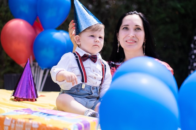 Zdjęcie matka i syn wyglądający uroczo w szelkach świętują balony z okazji pierwszych urodzin