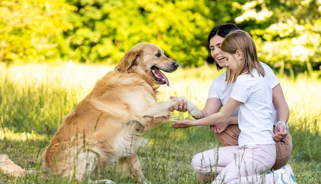 Matka i urocza córka bawią się z uroczym psem golden retriever na zewnątrz