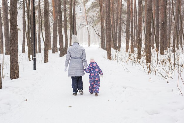 Matka idzie z córeczką w śnieżnym parku, widok z tyłu.