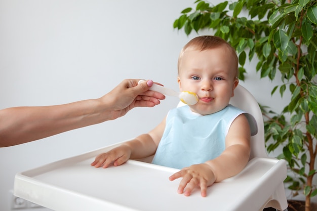 Matka Karmi łyżeczką Piękne Szczęśliwe Blond Dziecko W Niebieskim śliniaku