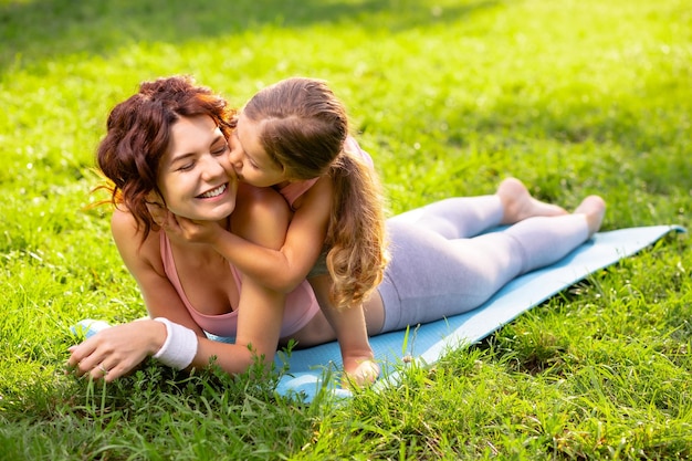 Matka leży na macie do jogi z córką na plecach w ciągu dnia