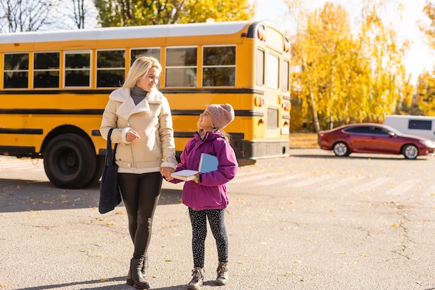 Zdjęcie matka odprowadza córkę do szkolnego autobusu przed szkołą podstawową.