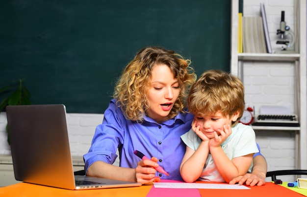 Matka pomaga synowi napisać lekcję mały uczeń z rodzicem w klasie szkolnej w szkole podstawowej