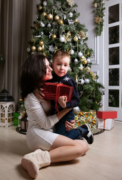 Matka przytula swojego szczęśliwego syna, który trzyma duże pudełko z prezentem bożonarodzeniowym
