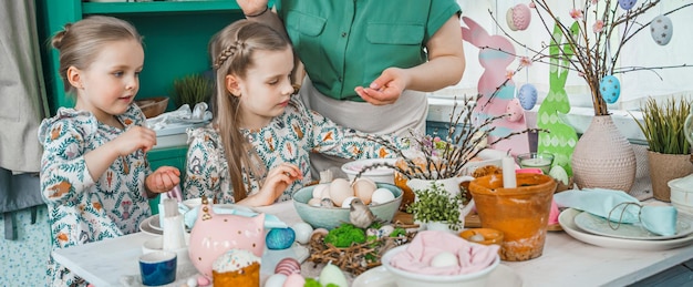 Zdjęcie matka sióstr dziewcząt przy stole z dekoracją wielkanocną uroczystość w kuchnipejzaż stołowy do domu święta wielkanocnerodzinny religijny tradycyjny świąteczny posiłek kolorowe ciasto jajeczne zabawne uszy królika