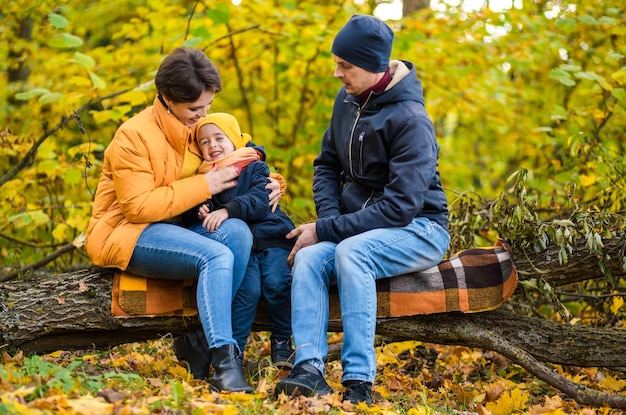 Matka tata i synek siedzą na pledach na kłodzie w jesiennym parku i spędzają razem czas