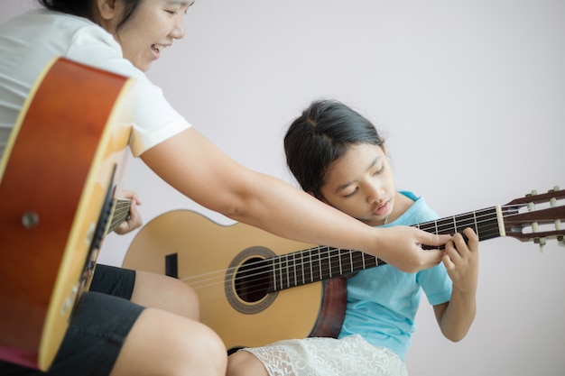 Matka uczy córkę ucząc się gry na akustycznej gitarze klasycznej dla jazzu i łatwego słuchania utworu. Wybierz ostrość płytkiej głębi ostrości