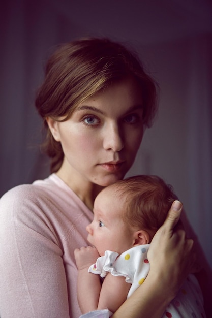 Matka w białej szlafroku trzyma małą nowo narodzoną córkę przy ścianie w sypialni