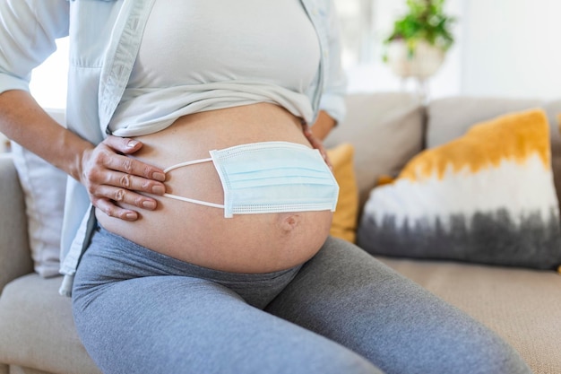 Matka w ciąży używa maski na brzuchu, aby chronić płód lub dziecko przed koronawirusem, covid19, zanieczyszczeniami, grypą lub pandemią. Kobieta w ciąży kwarantanna w domu.