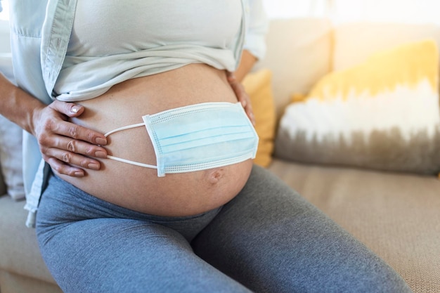 Matka w ciąży używa maski na brzuchu, aby chronić płód lub dziecko przed koronawirusem covid19 zanieczyszczeniem grypą lub pandemią Kwarantanna kobiet w ciąży w domu