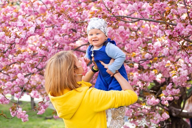 Matka w masce medycznej z małym synkiem bawiącym się w parku na drzewie sakura