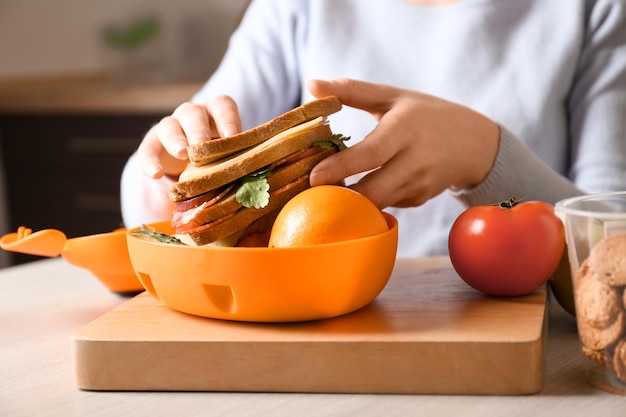 Zdjęcie matka wkłada jedzenie do szkolnego pudełka na lunch na stole