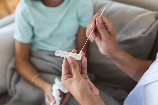 Matka wykonuje szybki test na Covid-19 w domu swojej chorej córce w domu. Matka wykonująca wymaz z nosa na swoim dziecku, biorąc przykład, aby przeanalizować, czy pacjent jest pozytywny na chorobę zakaźną