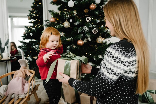 Matka wymienia prezenty z córką Rodzic i małe dziecko bawią się w pobliżu choinki Kochająca rodzina z prezentami w pokoju Rano przed świętami Bożego Narodzenia Portret mamy i dziecka z bliska