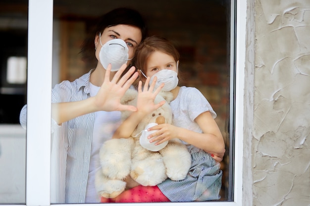 Matka z córką dziecko w masce patrząc z okna, koronawirusa.