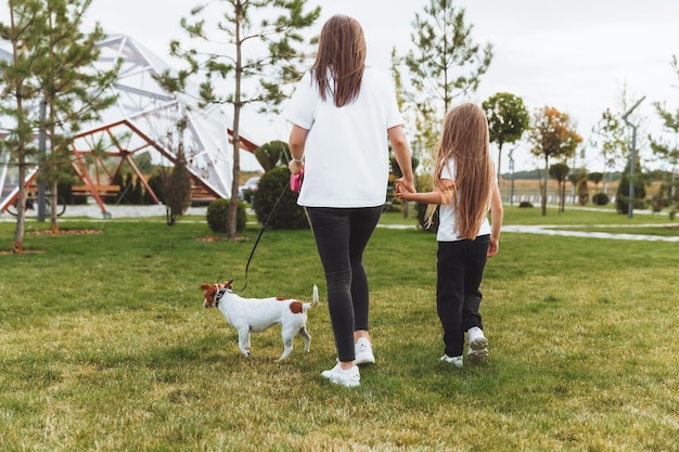 Matka z dzieckiem i psem Jack Russell terrier spacerują razem po parku kobieta i mała dziewczynka wyprowadzają psa