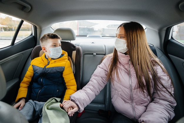 Matka z dzieckiem na tylnym siedzeniu samochodu w maskach jadąca do szpitala. Epidemia, kwarantanna.