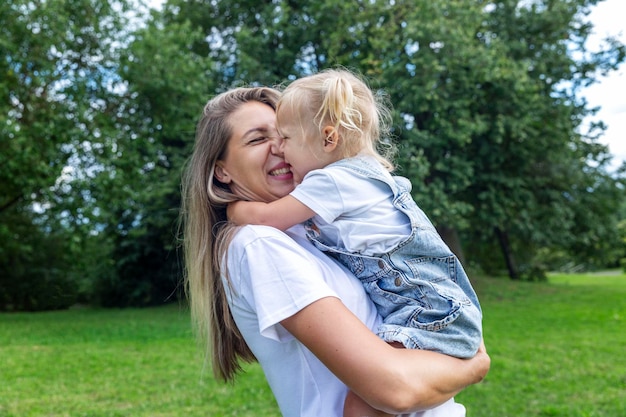 Matka z małą córką w ramionach śmieje się i przytula w letnim parku Miłość i czułość