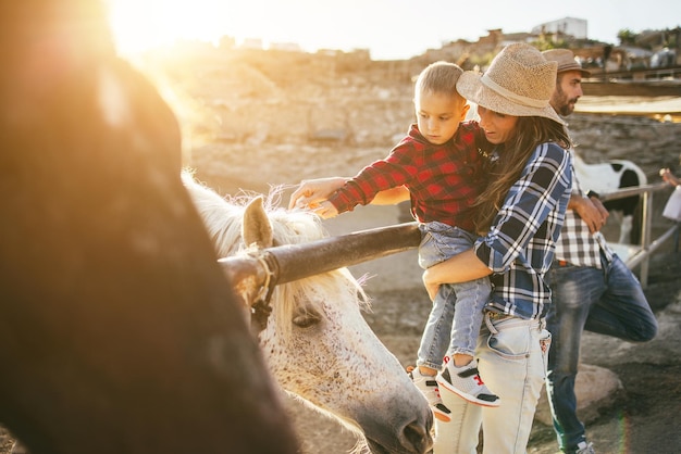 Matka z małym synkiem bawi się na koniu na farmie. Skup się na kapeluszu mamy