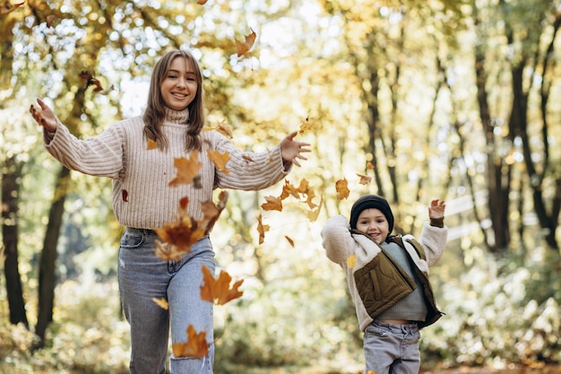 Matka z synem bawią się w jesiennym parku bawiąc się liśćmi