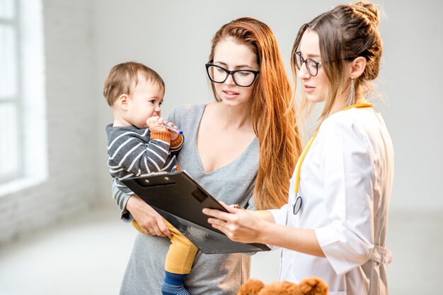 Zdjęcie matka z synkiem podczas konsultacji z młodą kobietą, pediatrą stojącą w białym gabinecie