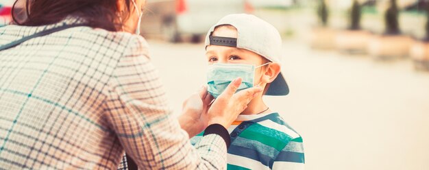 Zdjęcie matka zakłada sterylną maskę medyczną syna. matka, dziecko noszą maskę na twarz podczas koronawirusa, epidemii grypy. mama nakłada na syna maskę medyczną. dziecko i mama w masce medycznej na spacerze