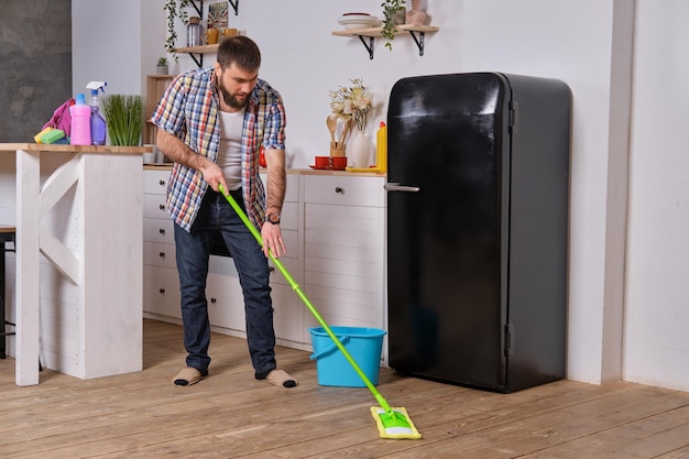 Mąż gospodyni sprząta kuchnię młody szczęśliwy mężczyzna z zielonym mopem myje podłogę