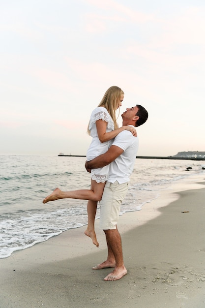 mąż trzyma żonę na plaży w pobliżu oceanu o zachodzie słońca. romantyczna para