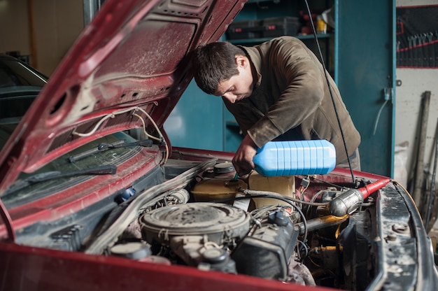 Mechanik mężczyzna pracownik nalewa antifreeze w układzie chłodniczym