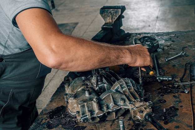 Mechanik naprawia skrzynię biegów na metalowym stole warsztatowym w warsztacie samochodowym Mechanik samochodowy w pracy