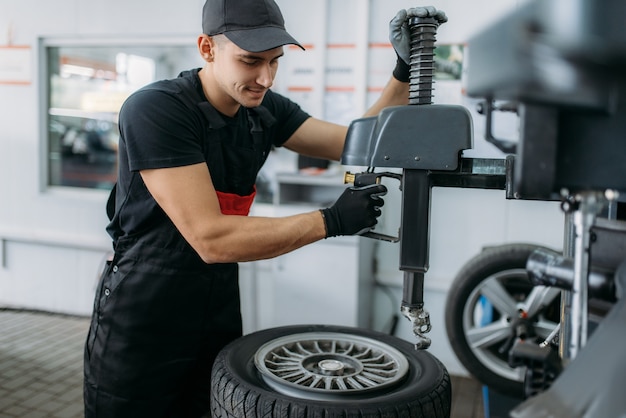 Zdjęcie mechanik naprawiający złamane koło na maszynie do montażu opon, usługa naprawy. mężczyzna naprawia oponę samochodową w garażu, inspekcja samochodu w warsztacie