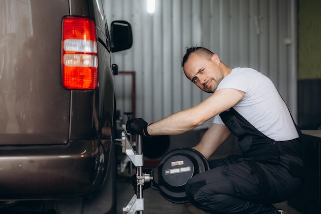 mechanik samochodowy instalujący czujnik podczas regulacji zawieszenia i wyrównania kół samochodu na stacji serwisowej naprawy